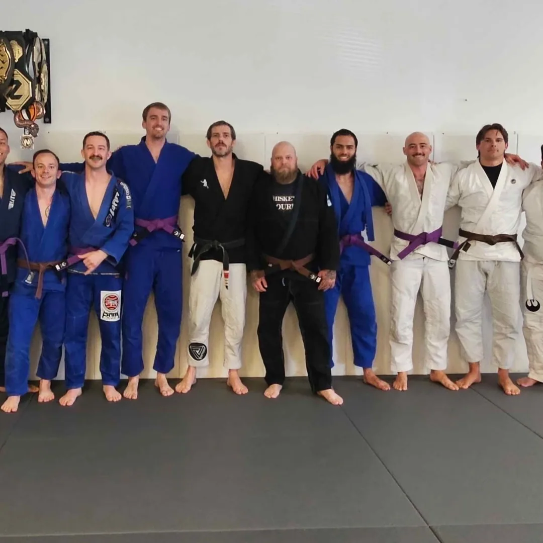 Adult gi jiu jitsu students and their coaches lined up on the mats in Norfolk