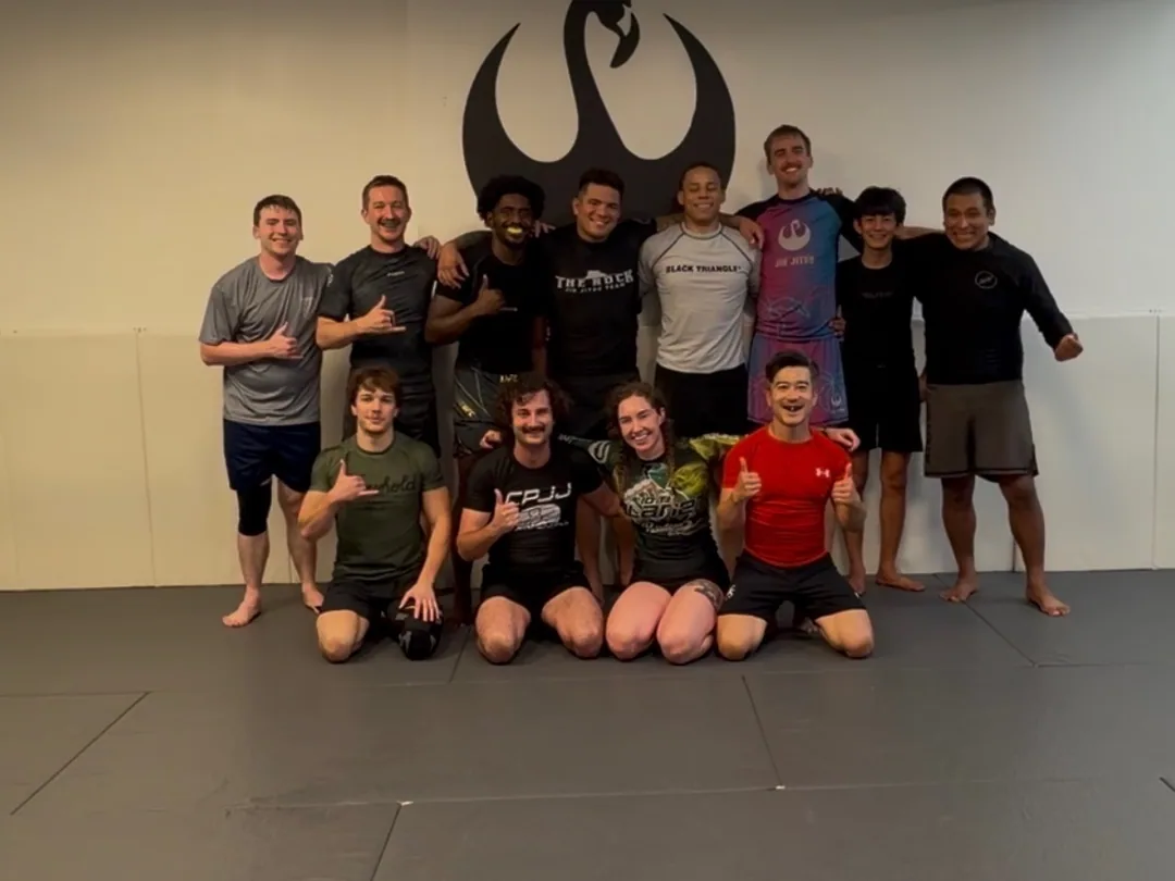 The adult no-gi class together in front of the academy wall logo in Norfolk