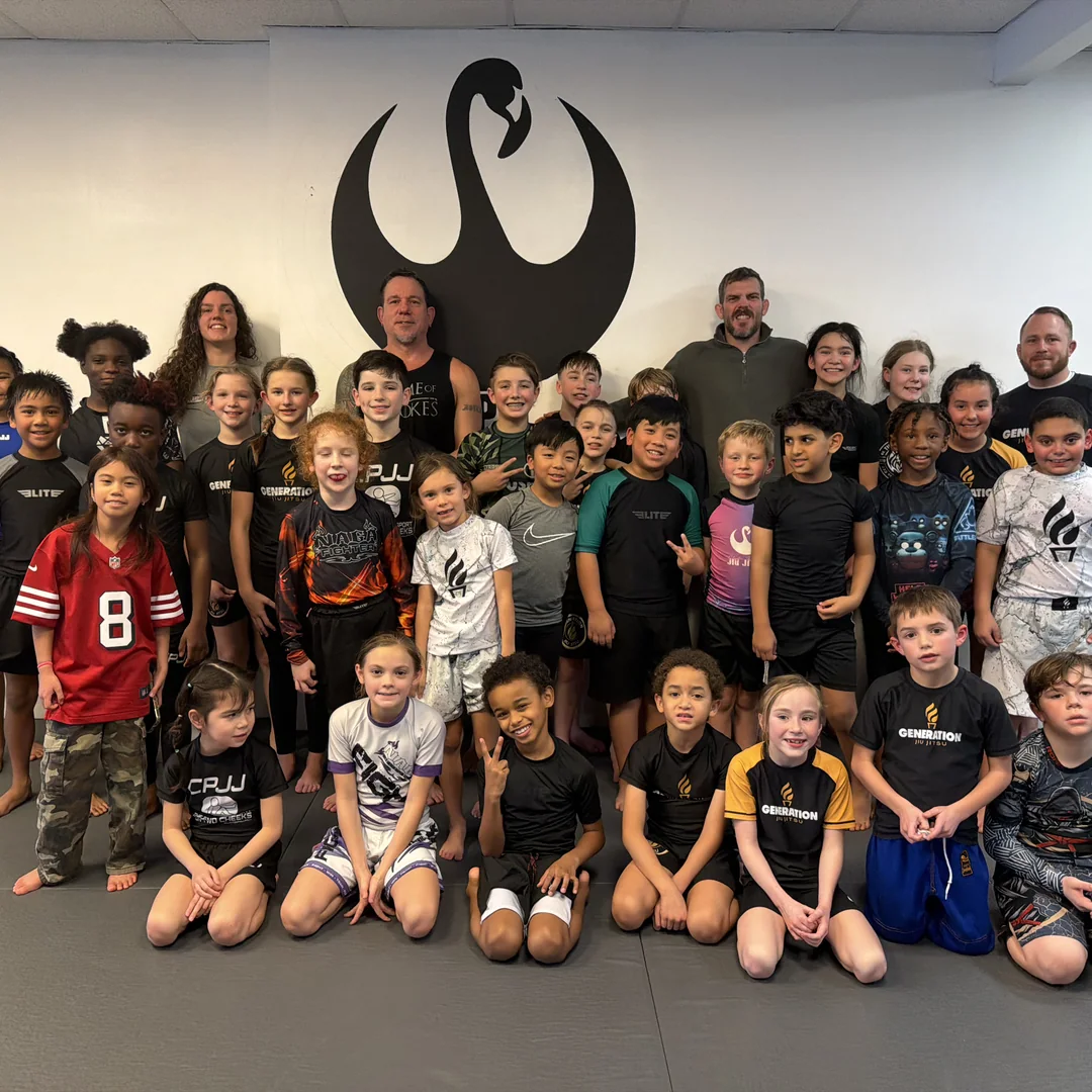 The CPJJ kids jiu jitsu class and their coaches gathered in front of the academy wall logo in Norfolk